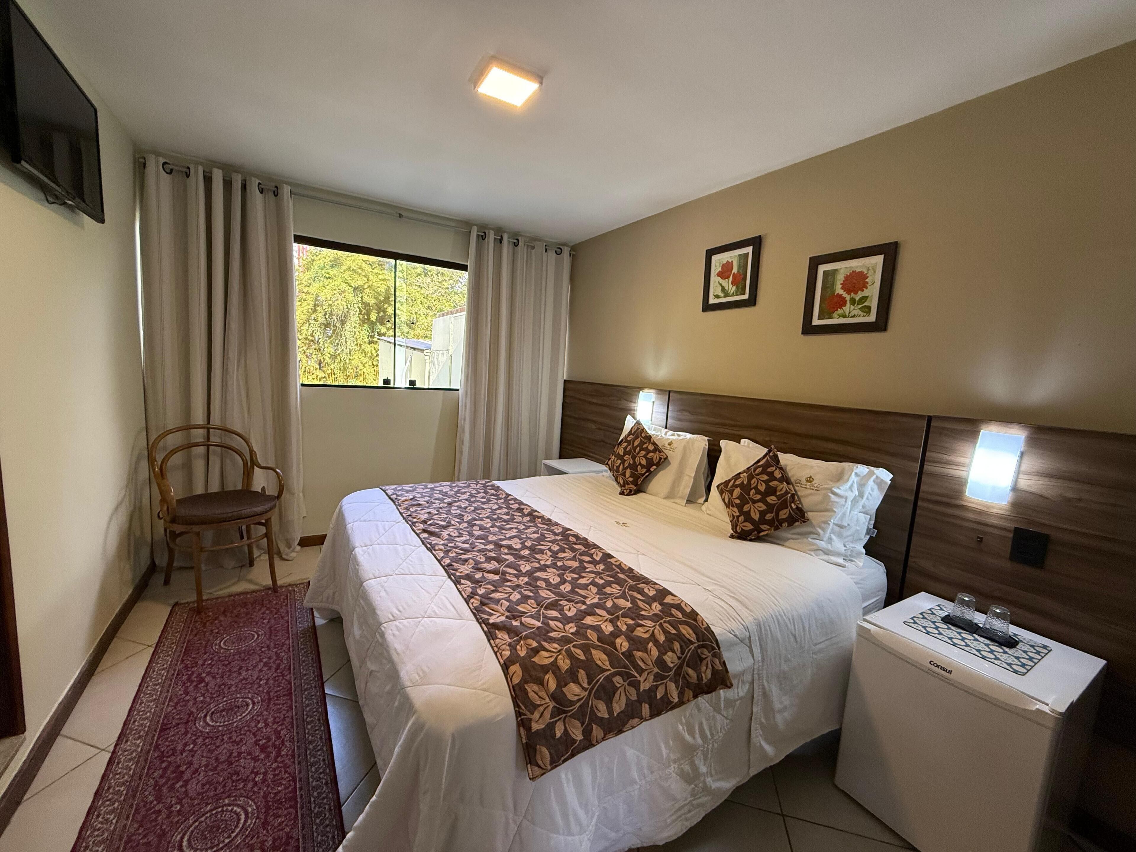 A hotel room with a bed, a chair, a nightstand, and a window with curtains.