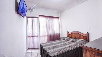 Un dormitorio con cama, televisor montado en la pared, ventilador de techo y ventana con cortinas.