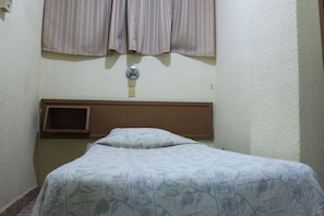 A small, single-bed room with a plain headboard, a window with curtains, and a wall-mounted light switch. - Hotel Plaza Aleman (León)