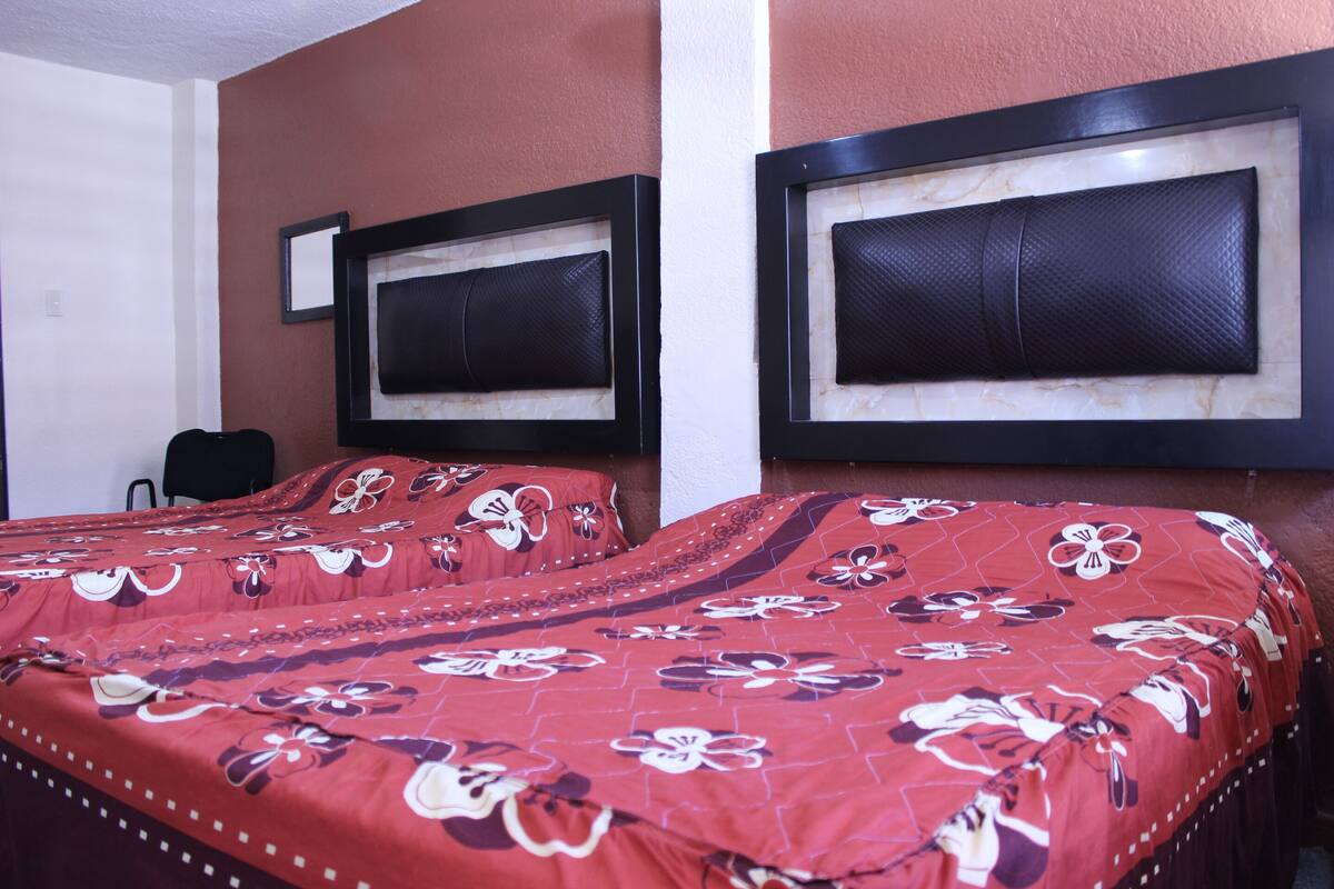 A hotel room with two beds, each with a headboard and a floral-patterned bedspread.