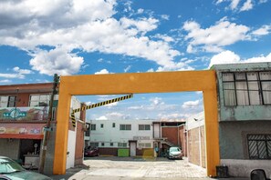 A building entrance with a yellow archway, a sign reading "Ocupie Su Espanol," and a visible street with parked cars. - Hotel Plaza Aleman (León)