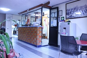 A reception area with a tiled wall, a reception desk, a refrigerator, and a seating area with chairs and a table.