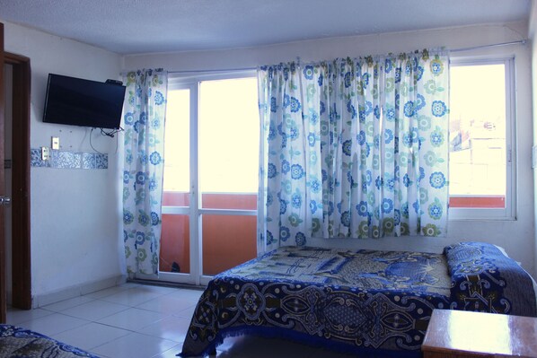 A bedroom with a bed, a TV mounted on the wall, and a window with curtains.