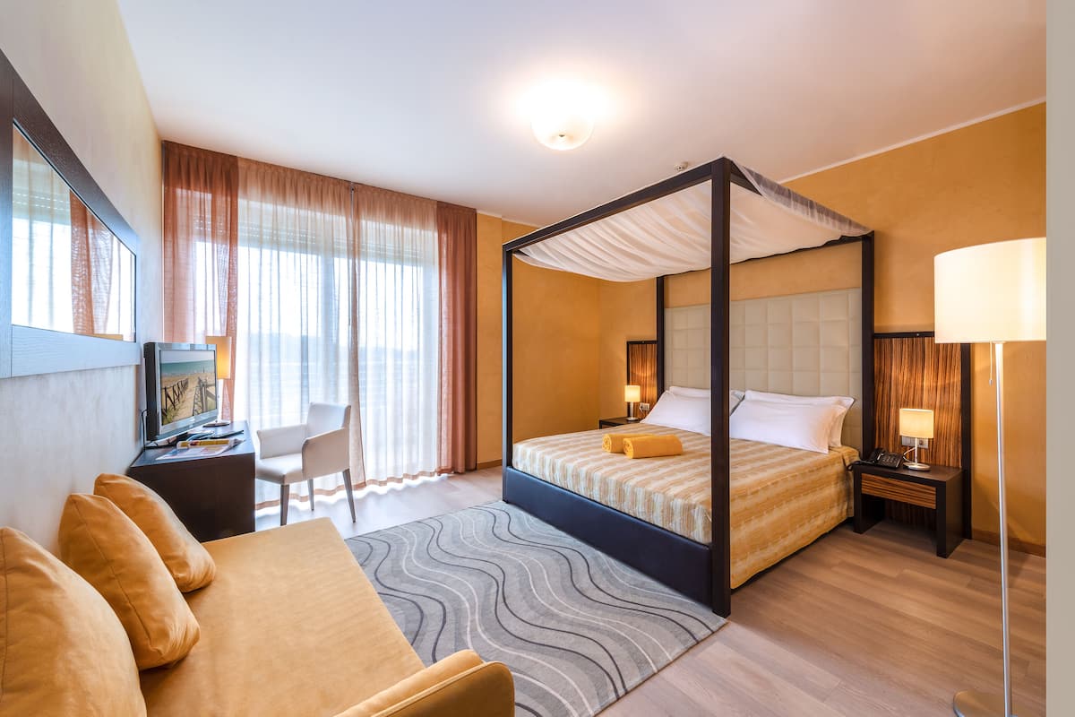Een hemelbed met hoofdbord, een bureau met stoel, een bank en een lamp.