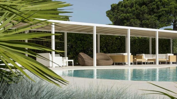 A pool area with a covered seating area, lounge chairs, and a large tree in the background. - Hotel San Marco (San Michele al Tagliamento)