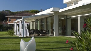 A modern building with a covered outdoor seating area, a well-maintained lawn, and a distinctive white sculpture. - Hotel San Marco (San Michele al Tagliamento)