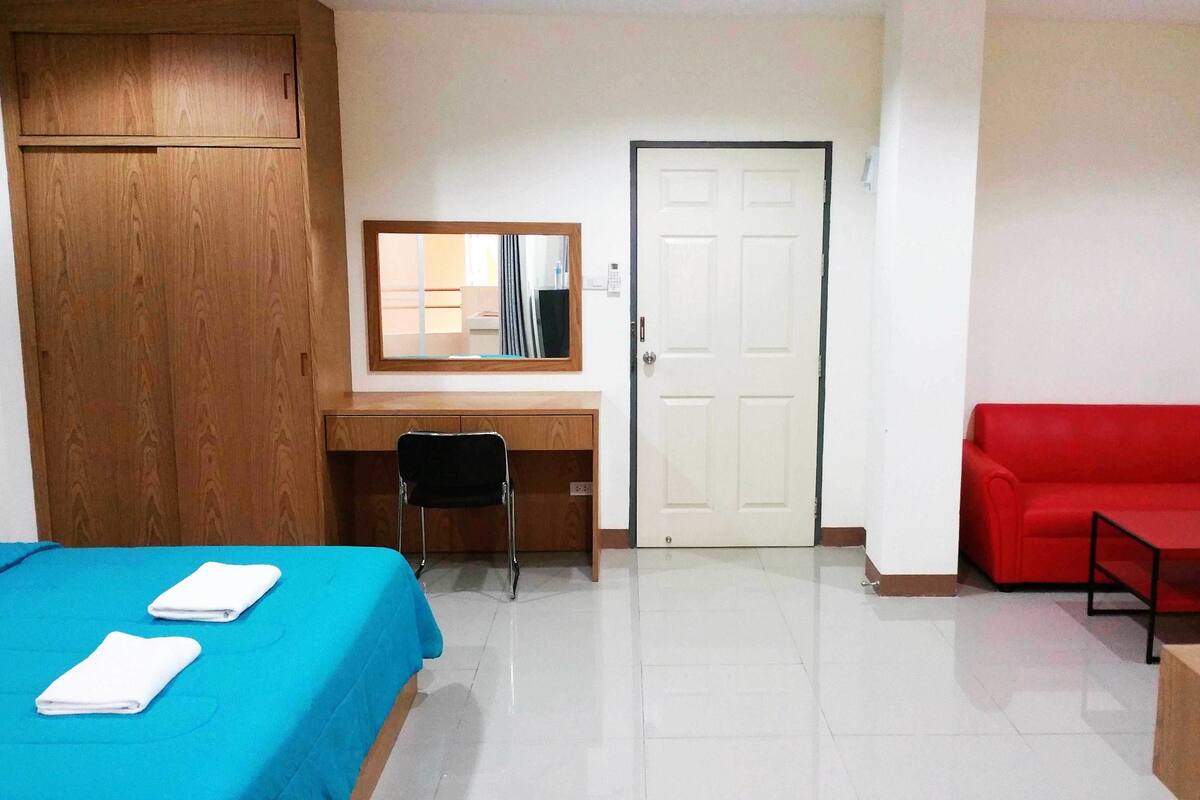A room with a bed, a desk, a chair, a red sofa, and a door.