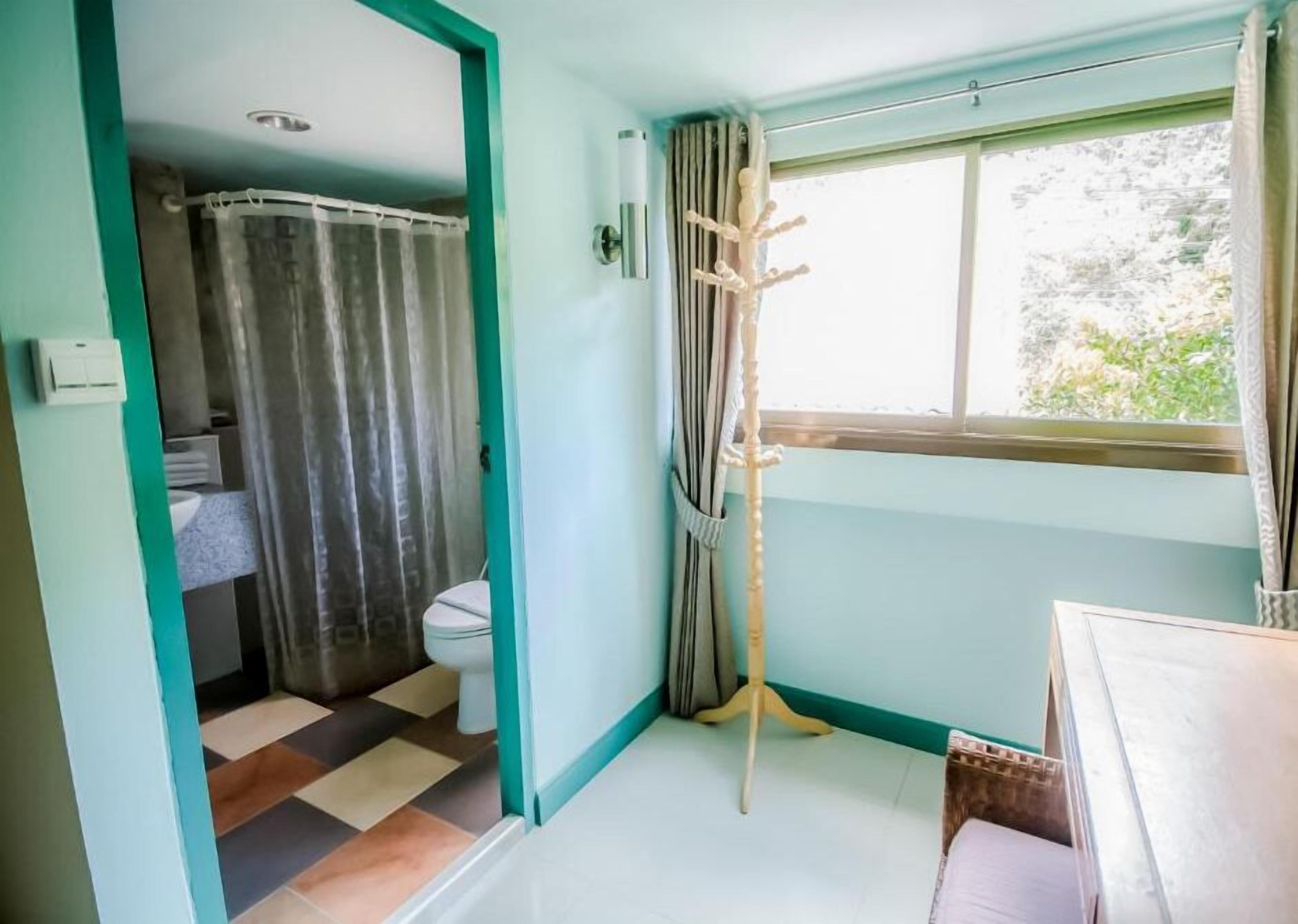 Un baño con inodoro, cortina de ducha y ventana con cortinas.