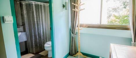 Un baño con inodoro, cortina de ducha y ventana con cortinas.