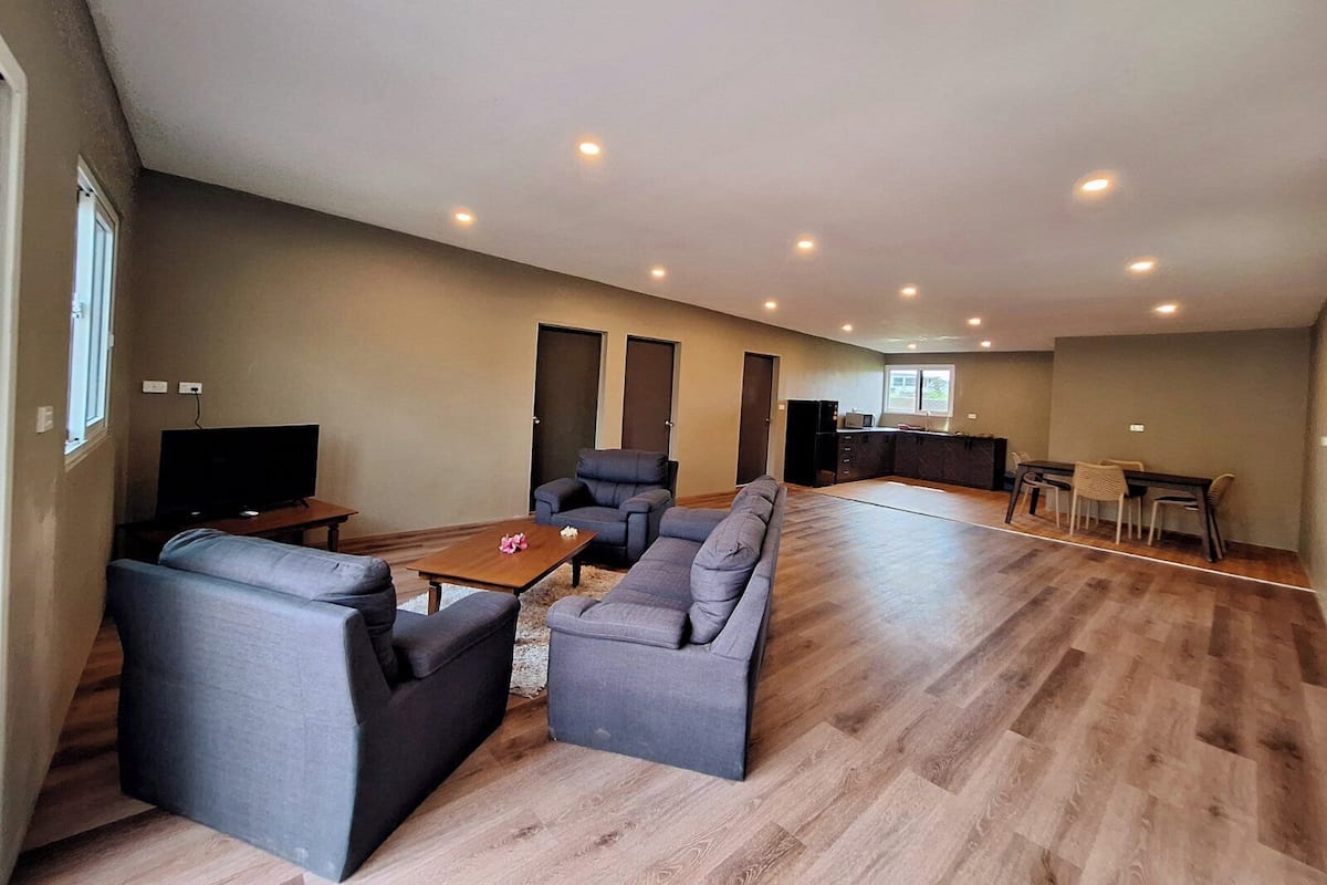 A spacious living area with a sofa set, a coffee table, and a TV. There is a kitchen area with a dining table and chairs.