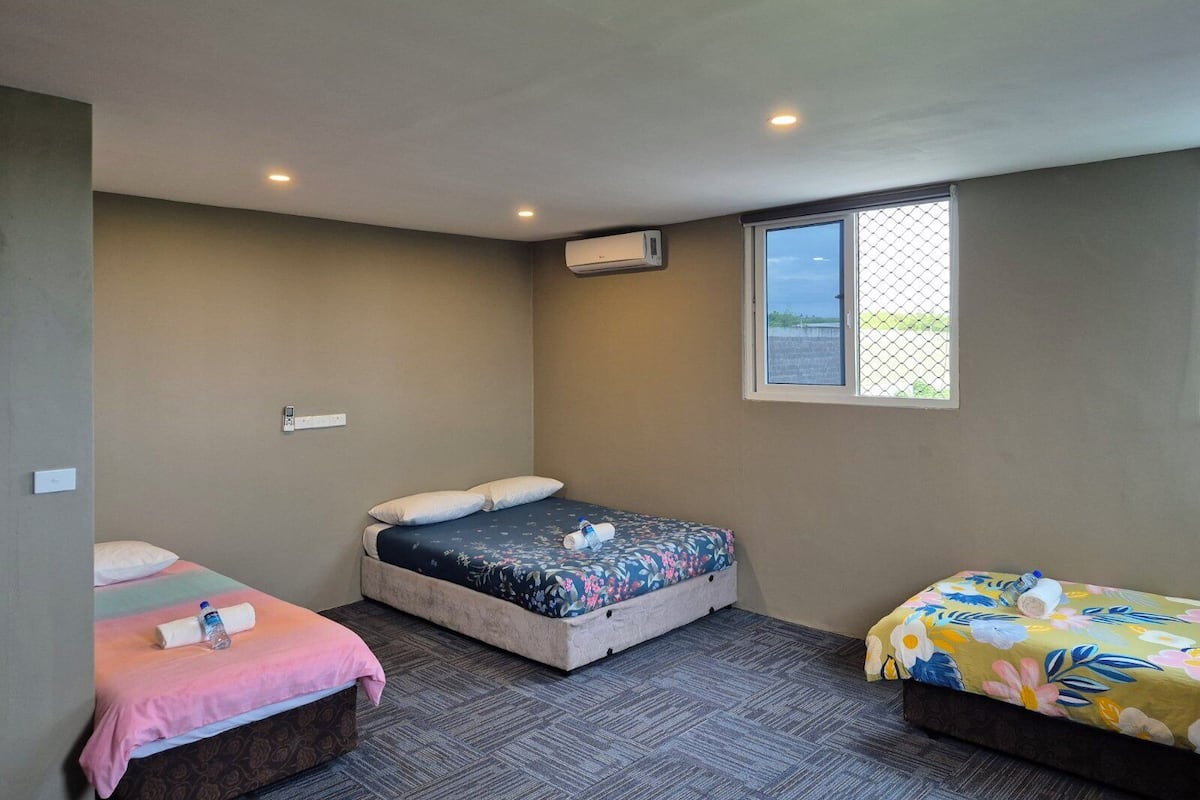A room with three beds, a window with a view, and an air conditioning unit.