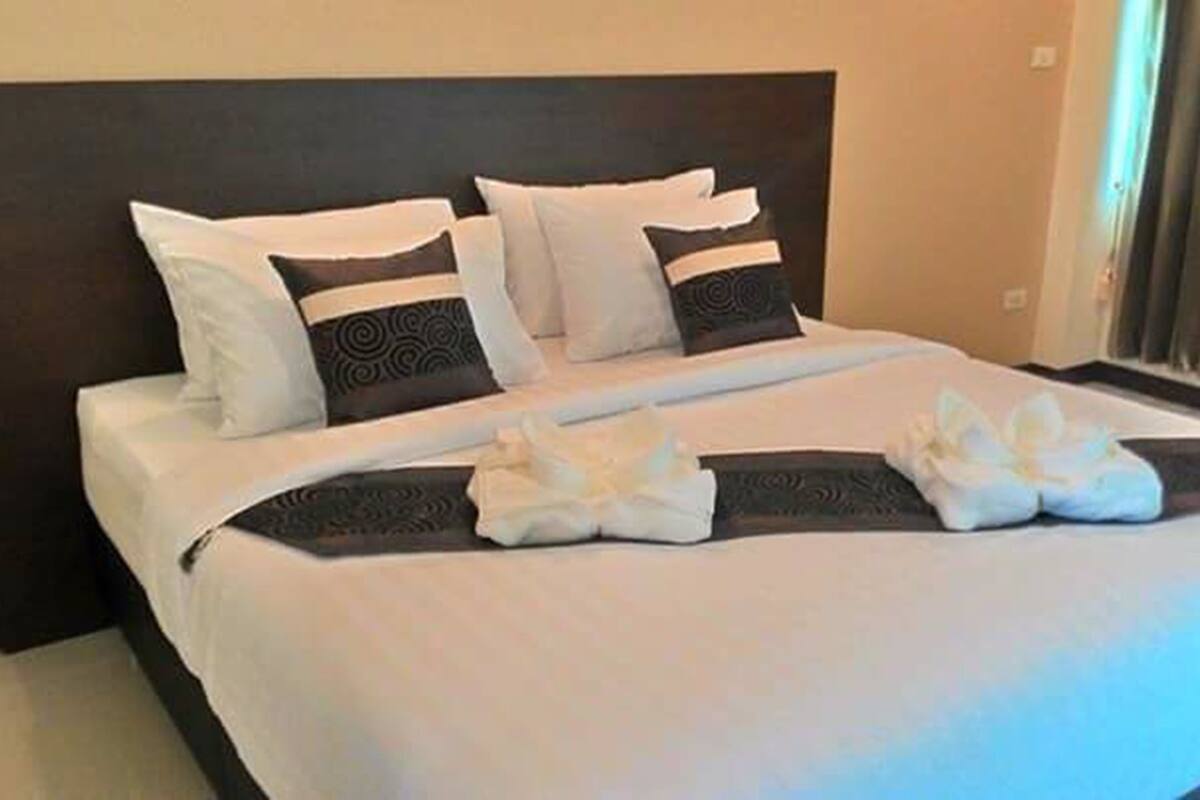 A neatly made bed with white and dark pillows, a decorative pillow with a circular pattern, and a towel arrangement on the bed.