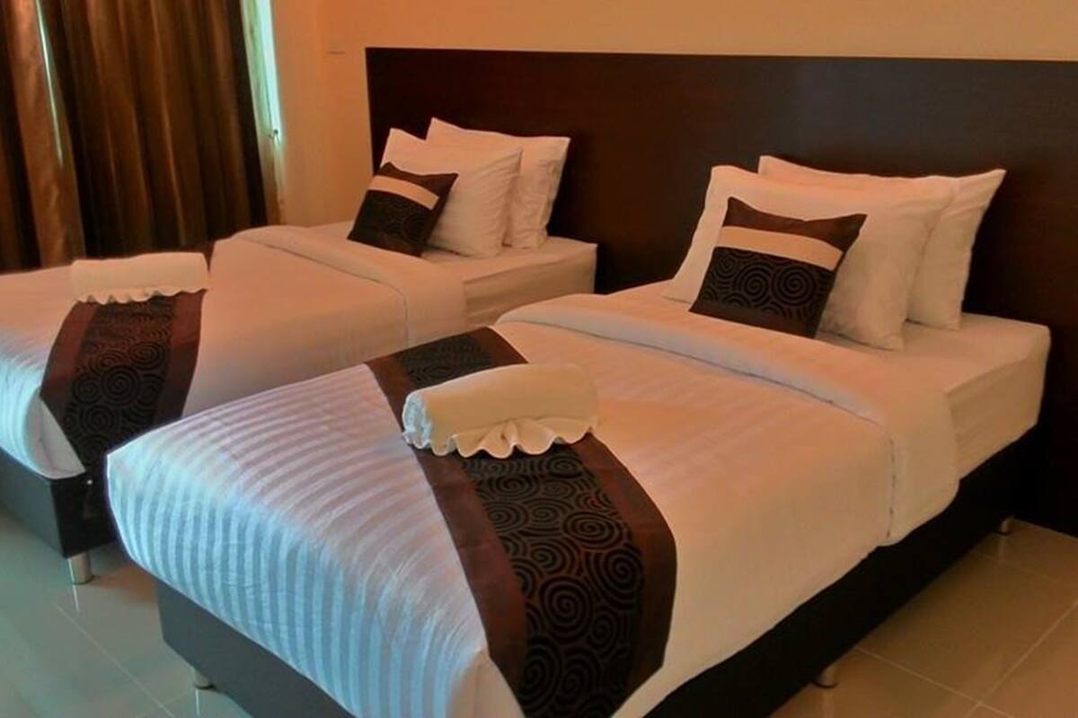 Two twin beds with white linens and dark patterned pillows, a wooden headboard, and a dark curtain in the background.