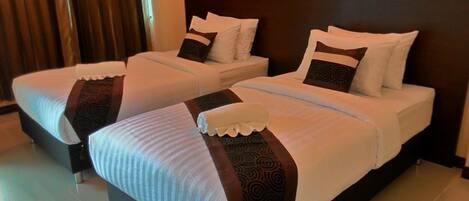 Dos camas individuales con sábanas blancas y almohadas oscuras estampadas, un cabecero de madera y una cortina oscura al fondo.