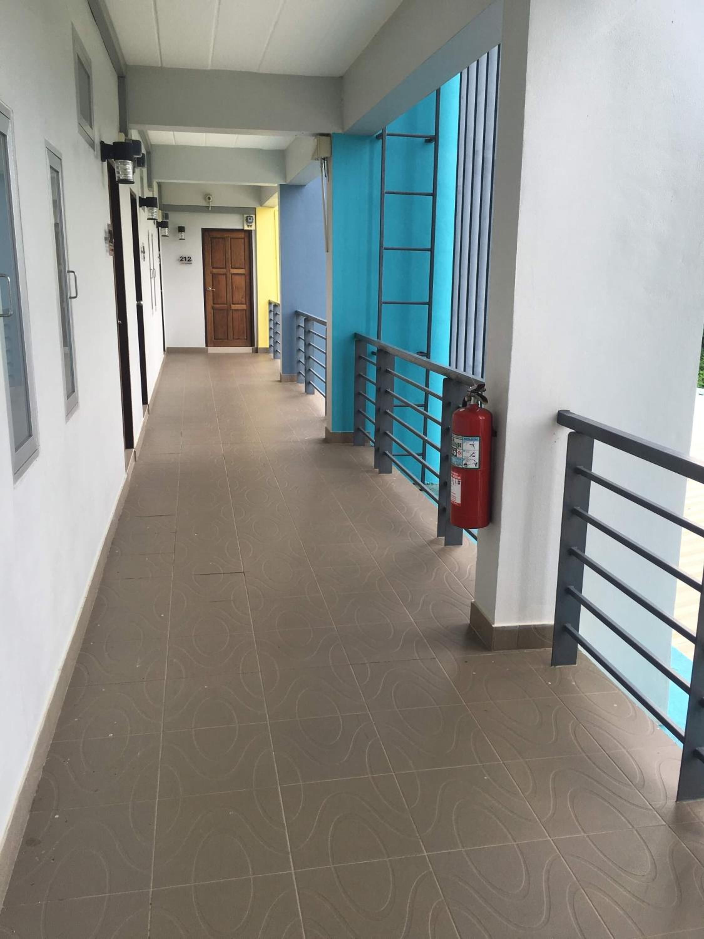 A long, narrow corridor with patterned floor tiles, a fire extinguisher mounted on the wall, and a door at the end.