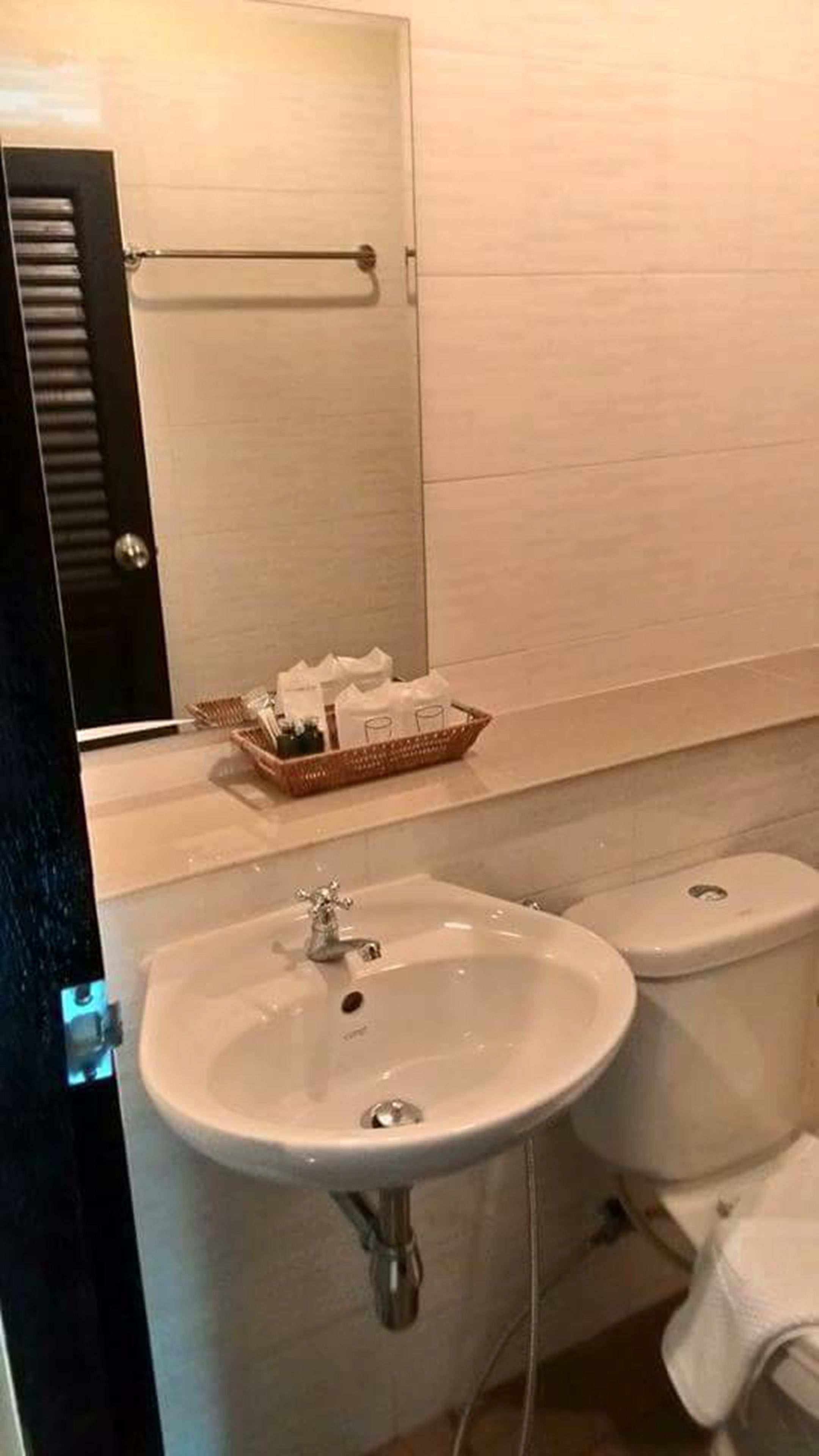 Un baño con lavamanos, inodoro y una cesta de artículos de aseo sobre el mostrador.