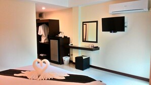 Una habitación de hotel con una cama, una tocadora con espejo, un televisor montado en la pared y un armario.