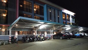 Un edificio con zona de estacionamiento techada y varias motocicletas y automóviles estacionados.
