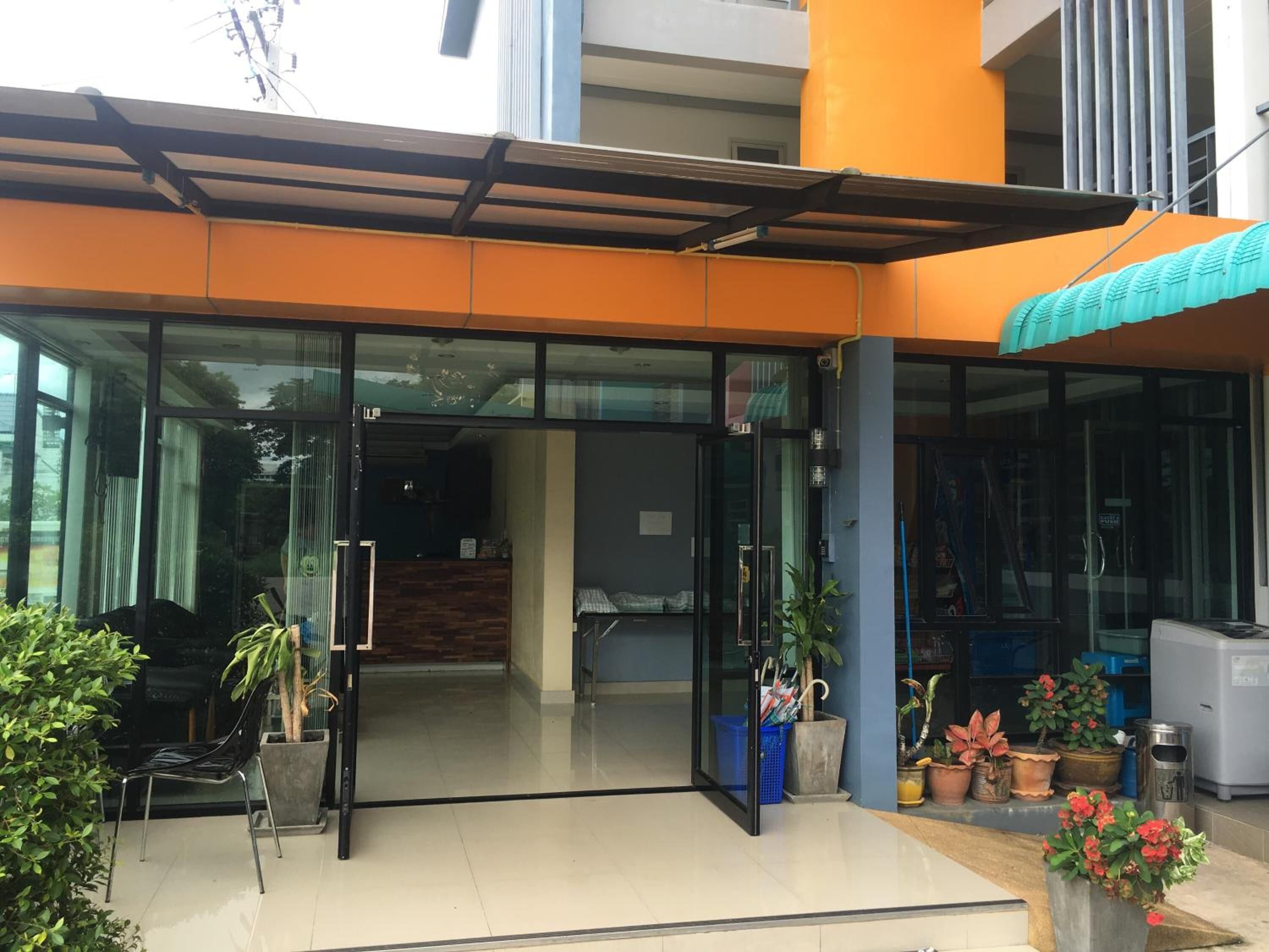 L’entrée d’un hôtel avec une porte en verre, un espace d’attente abrité et des plantes en pot à l’extérieur.