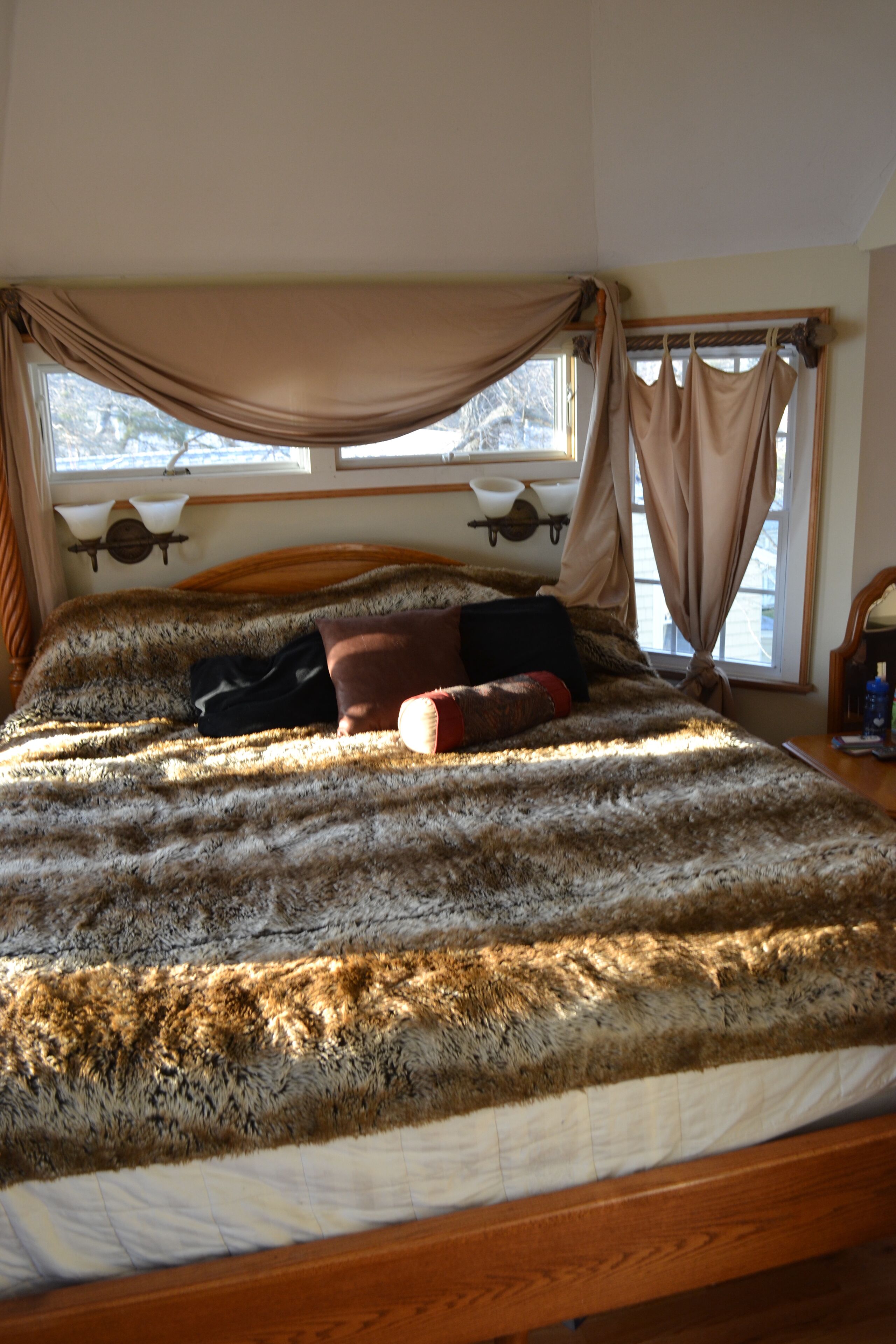A bed with a fur-like cover, a wooden headboard, and a window with curtains.