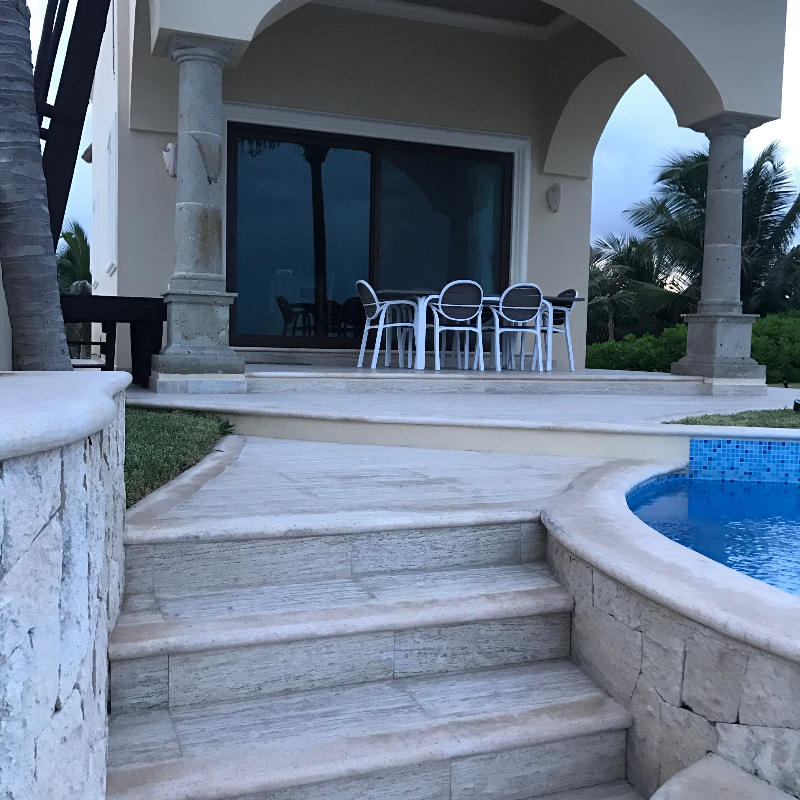 A pool area with steps leading to a covered patio with outdoor furniture.