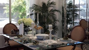 Un comedor con una mesa de vidrio, sillas, una araña y vistas al exterior.