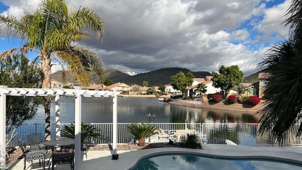 Zona de piscina con un pérgola, sillas y vistas a un lago y montañas.