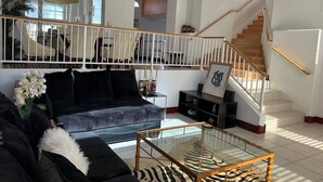Un salón amplio con un sofá negro, una mesa de centro de cristal y una escalera que sube a un piso superior.