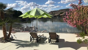 Un patio con dos sillas y una mesa, una sombrilla verde y vista a un lago con barcos.