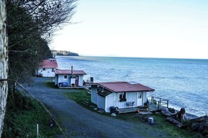 A row of small cabins with red roofs by a lake, connected by a gravel path.