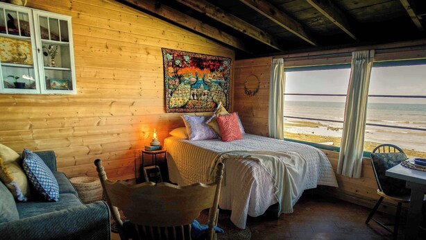 Um quarto de cabana aconchegante com uma cama, duas cadeiras, uma mesa e vista para a praia.