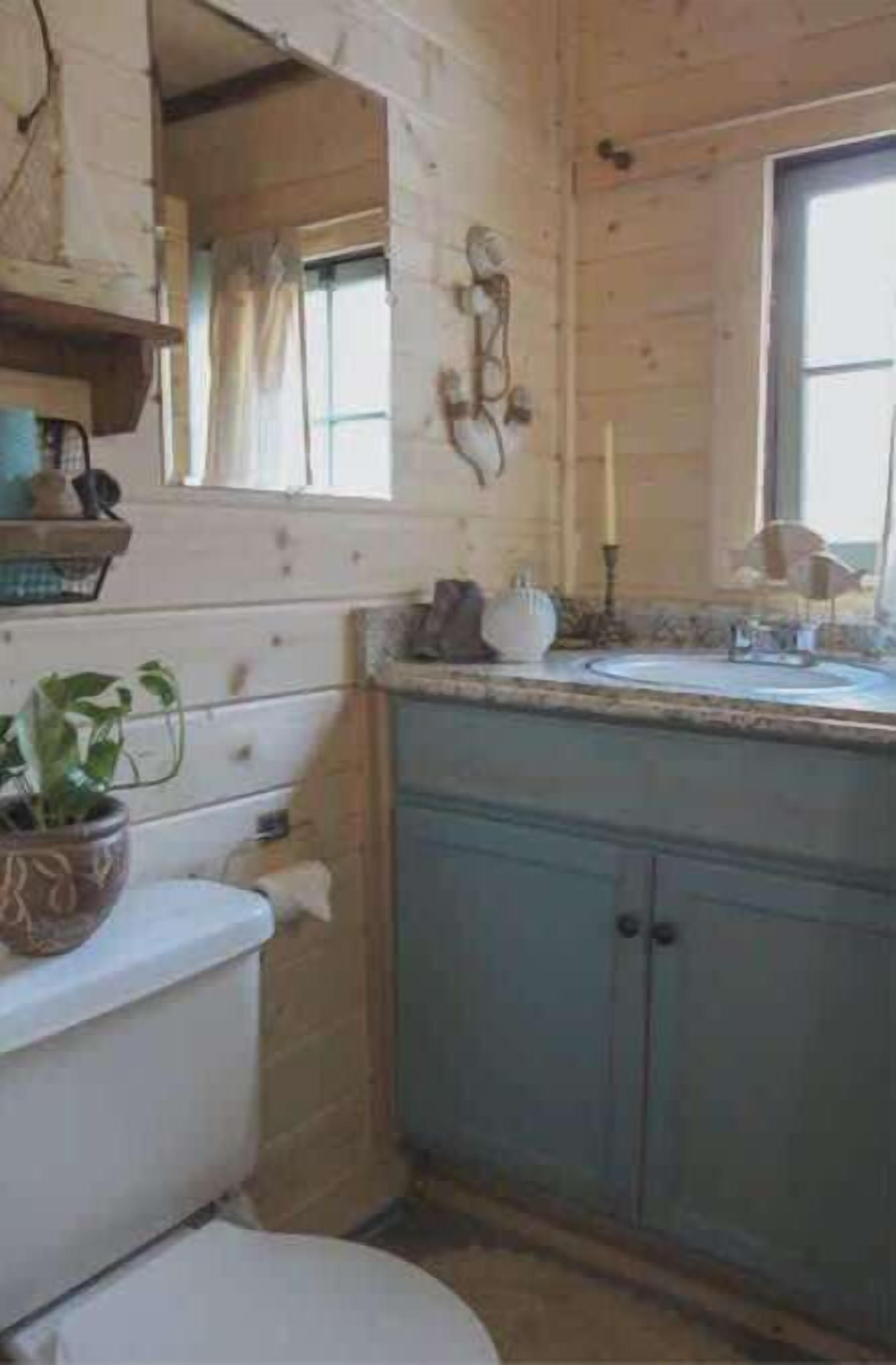 Un baño pequeño y rústico con pared de madera, inodoro, lavabo con espejo y ventana.