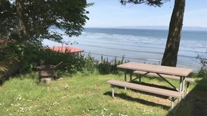 Ein Picknicktisch und eine Feuerstelle in einer grünen Wiese mit Blick aufs Meer.