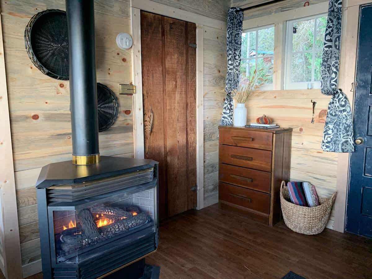A cozy cabin interior with a wood-burning stove, a wooden door, a dresser, and a basket by the door.