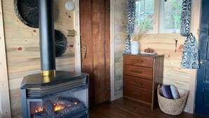 Interior acogedor de una cabaña con una estufa de leña, una puerta de madera, un aparador y una cesta junto a la puerta.