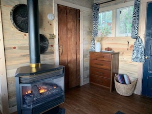 Interior acogedor de una cabaña con una estufa de leña, una puerta de madera, un aparador y una cesta junto a la puerta.