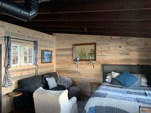 Una habitación acogedora de estilo cabaña, con cama, dos sofás, una mesita y una ventana con cortinas.