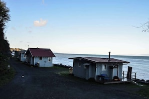 Una proprietà costiera con due piccoli chalet, uno con tetto rosso e l'altro con tetto grigio, entrambi con portici e vista sul mare.