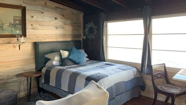 A cozy bedroom with a bed, a chair, a small table, and a window with curtains.