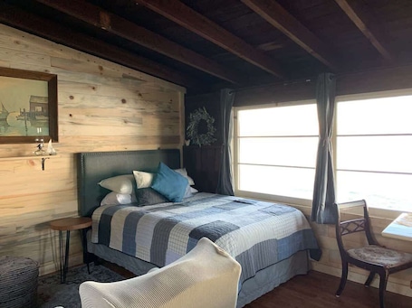 A cozy bedroom with a bed, a chair, a small table, and a window with curtains.