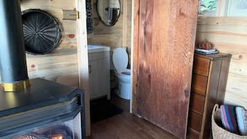 A rustic cabin interior with a wood-burning stove, a toilet, and a wooden door.
