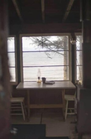 Ein Zimmer mit großem Fenster und Blick auf ein Gewässer, einem Holztisch und zwei Stühlen.