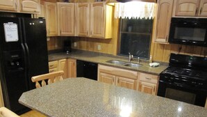 A kitchen with granite countertops, wooden cabinets, a black refrigerator, a stainless steel sink, and a black stove.