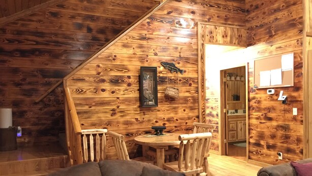 A cozy cabin interior with a wooden interior, a dining table with chairs, and a staircase leading to an upper level.