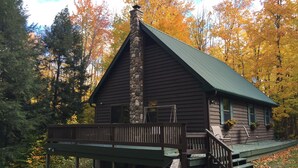 A cabin with a stone chimney, wooden deck, and a porch.