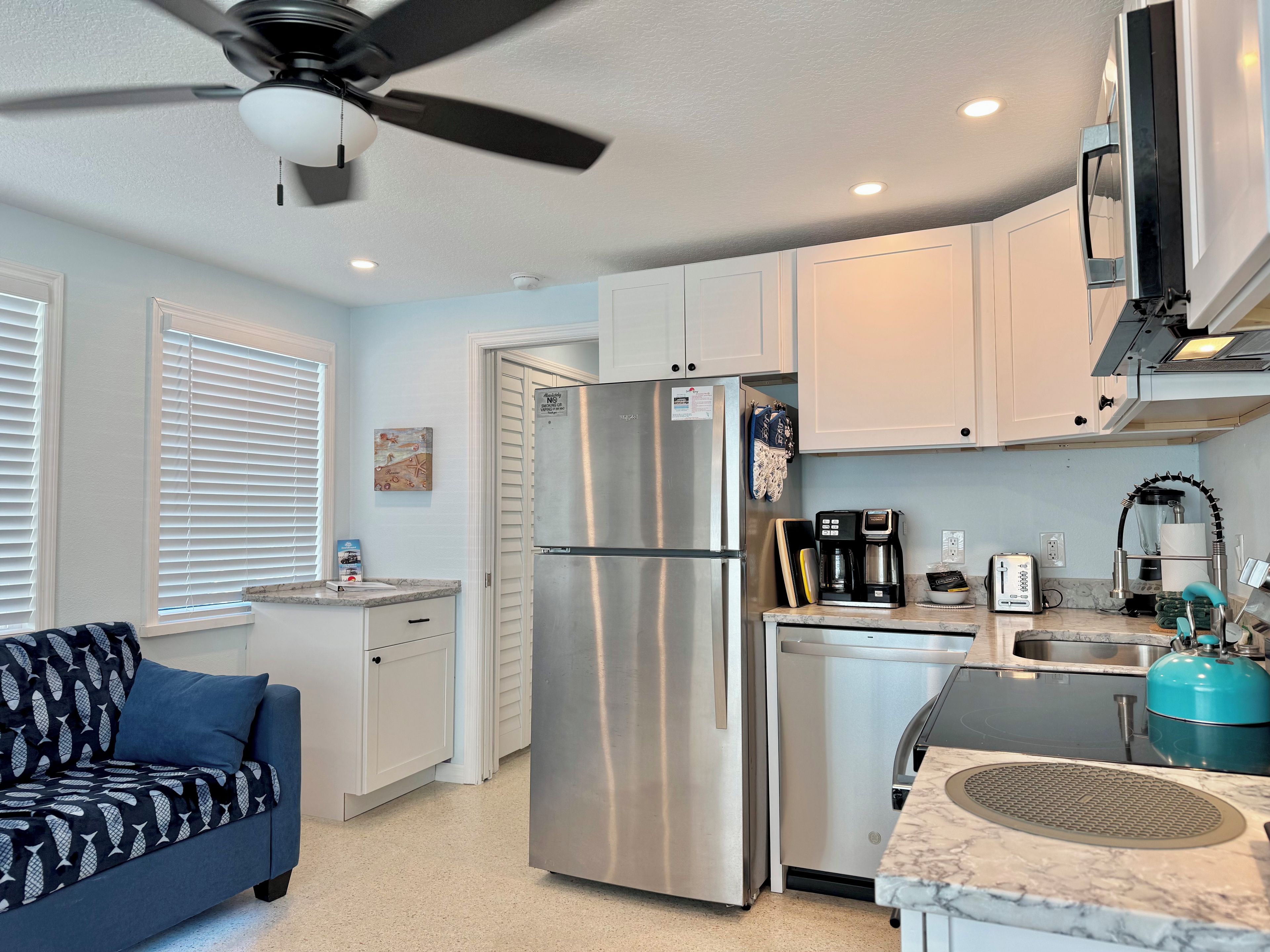 A compact kitchen with a refrigerator, coffee maker, and a blue kettle.