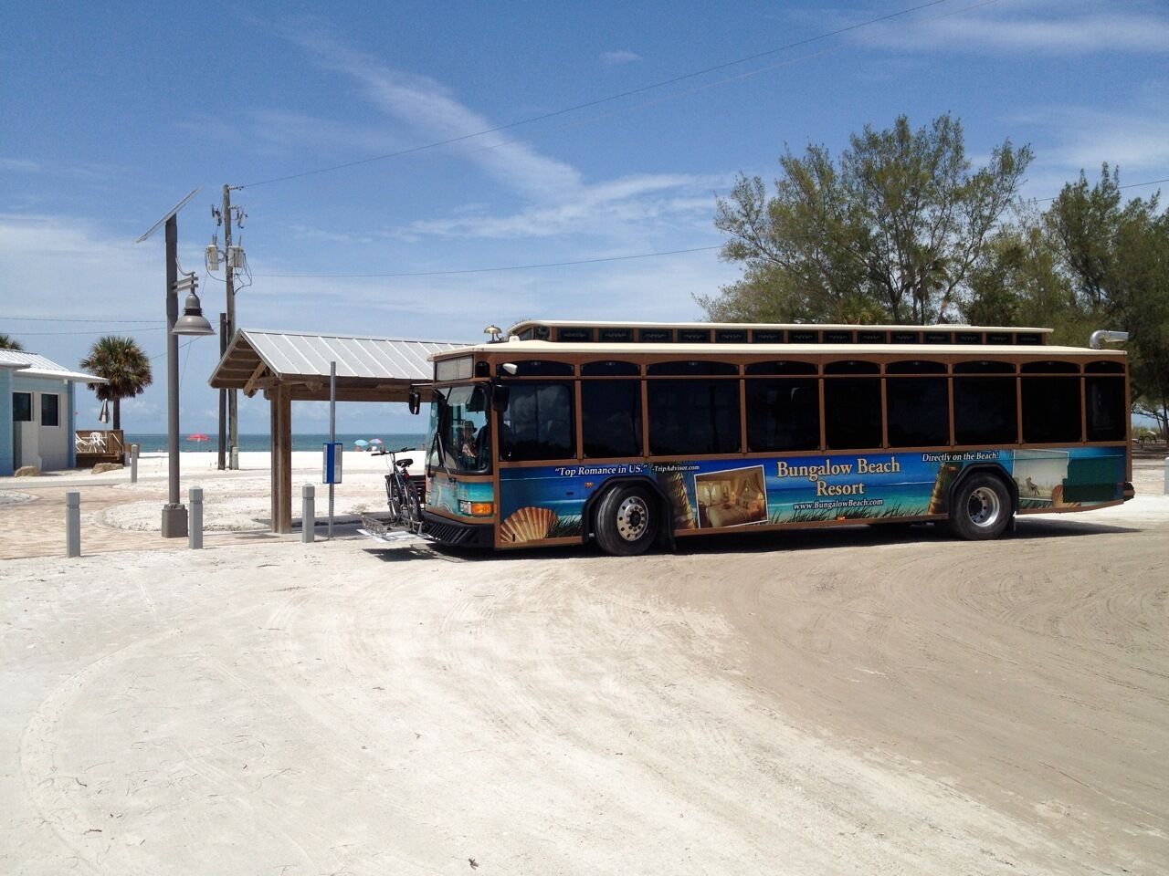 Un autobús estacionado en una zona arenosa con un anuncio de un complejo turístico de playa en su lateral.