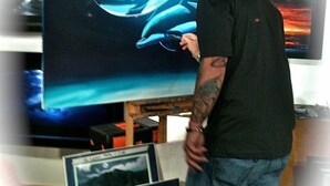 Un hombre con camisa y jeans de color negro, de pie frente a un televisor de pantalla plana grande que muestra una imagen de delfín.