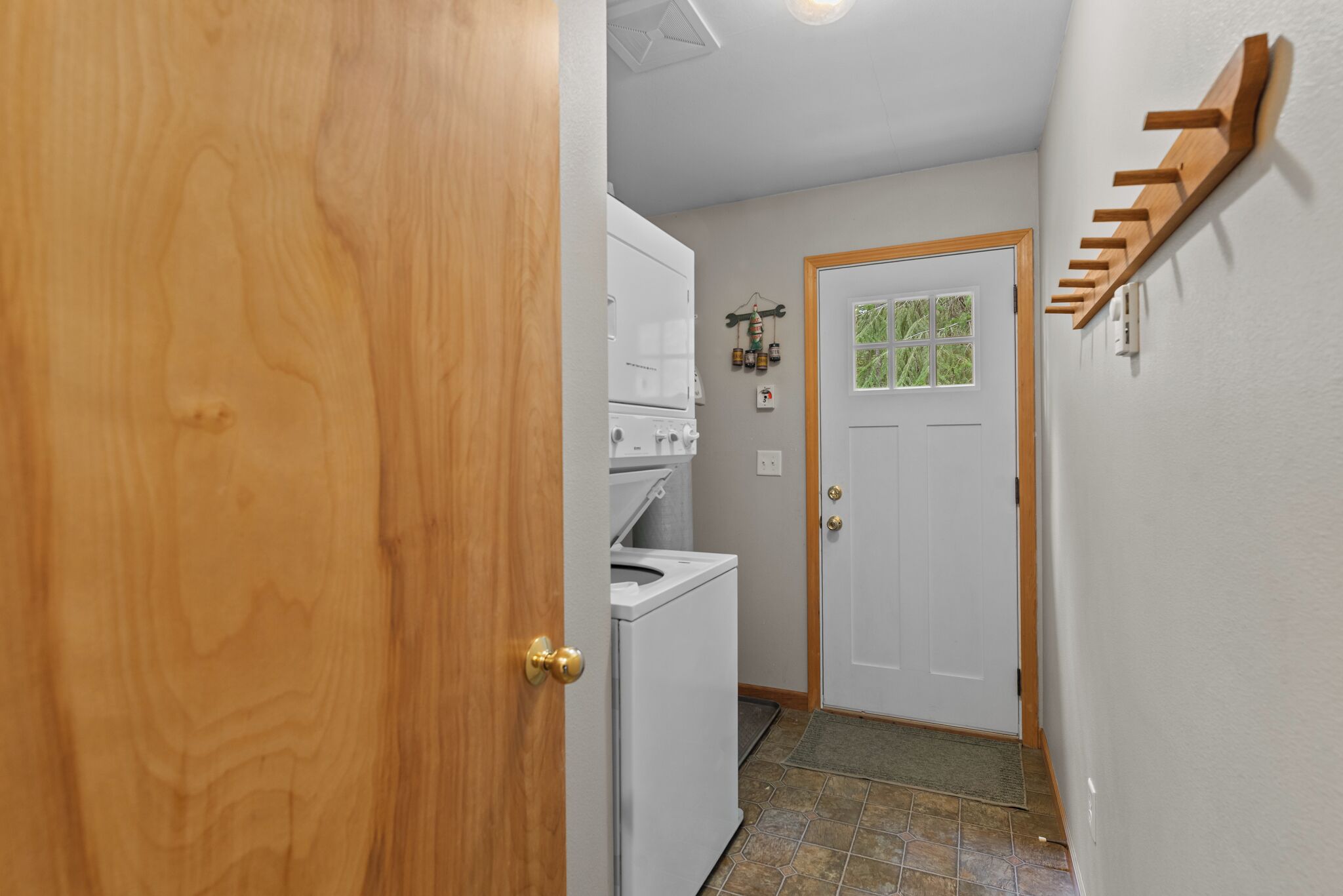 A laundry room with a washer and dryer, a door with a doormat, and a coat rack on the wall.