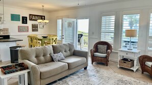 A spacious living room with a sofa, a dining area, and a balcony with a view.